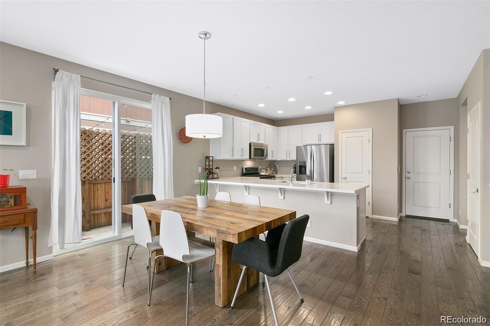 Open-plan kitchen and dining area with a white island and rustic wood table beside sliding glass doors.