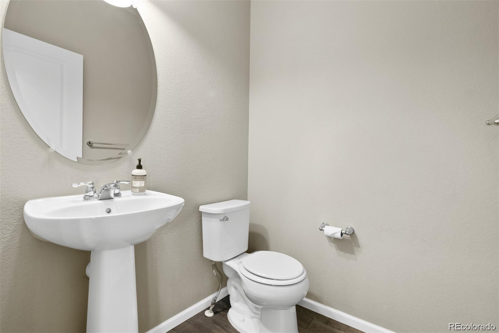Bathroom with a white pedestal sink, round mirror, and toilet.