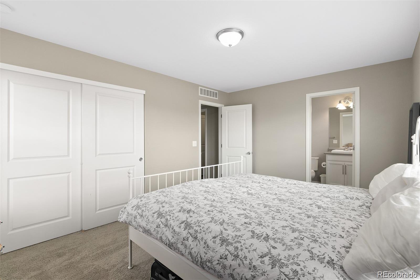 Bedroom with a white metal bed, floral bedding, sliding closet doors, and an en-suite bathroom doorway.