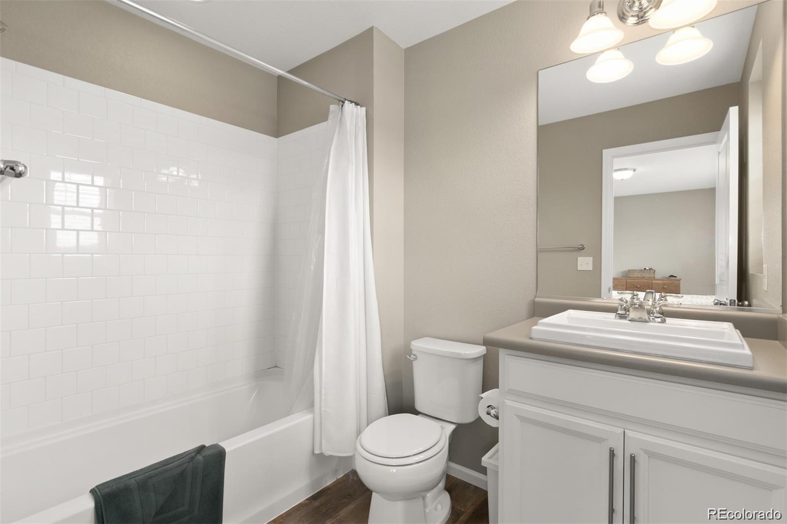 Bathroom with white subway-tile tub surround, shower curtain, toilet, and white vanity.