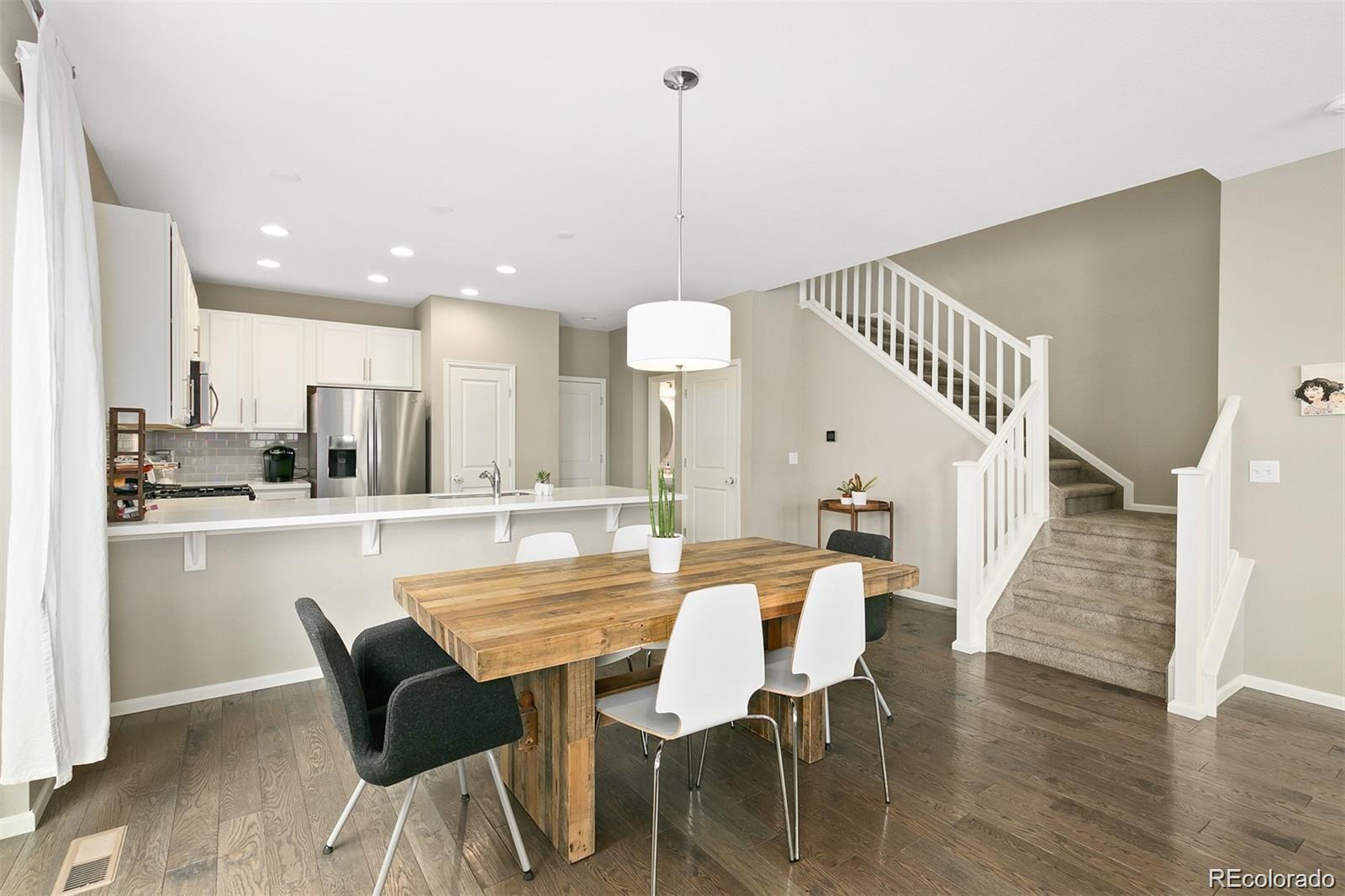 Open-plan kitchen and dining area with a rustic wooden table and carpeted staircase.