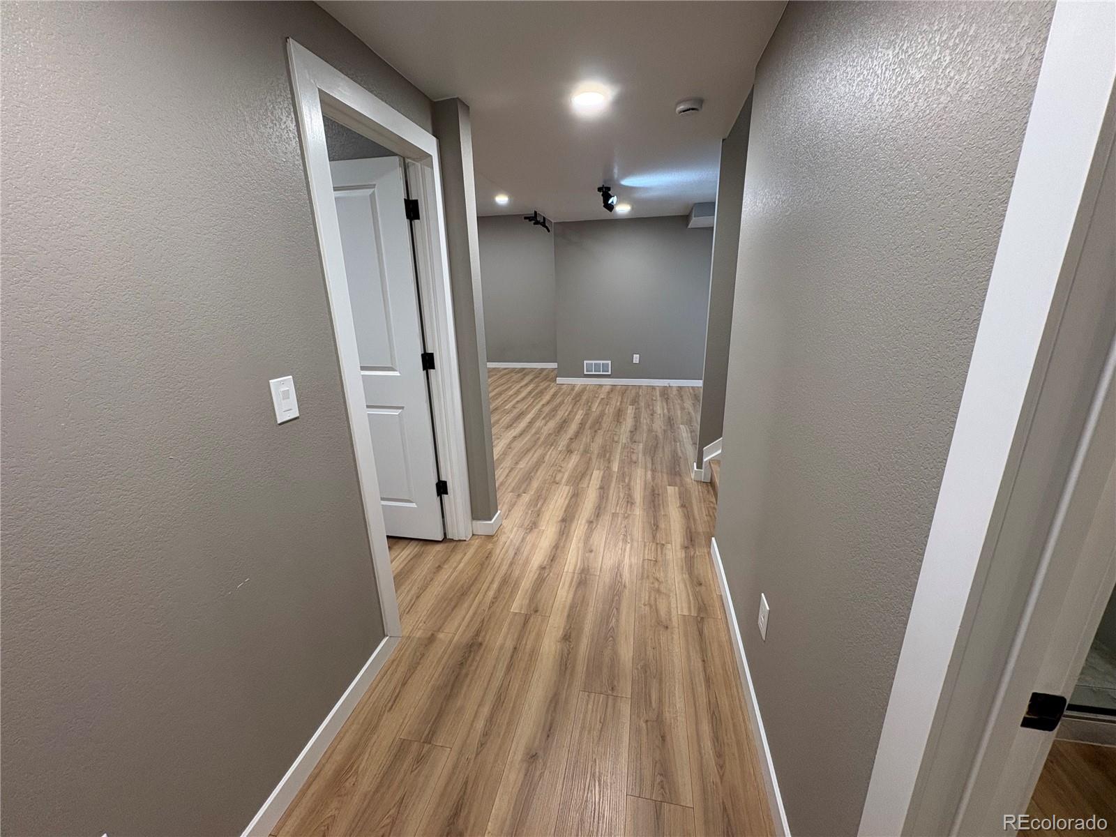 Unfurnished hallway with wood-look flooring leading to an empty gray room.