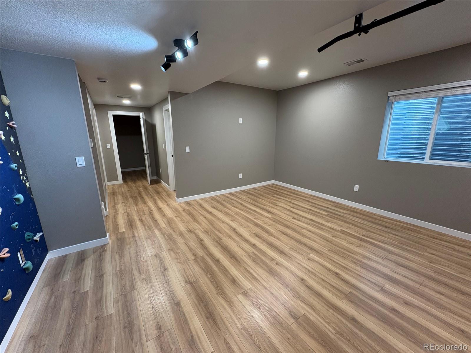 Empty room with wood-look flooring, a blue climbing wall, and a garage-door track.