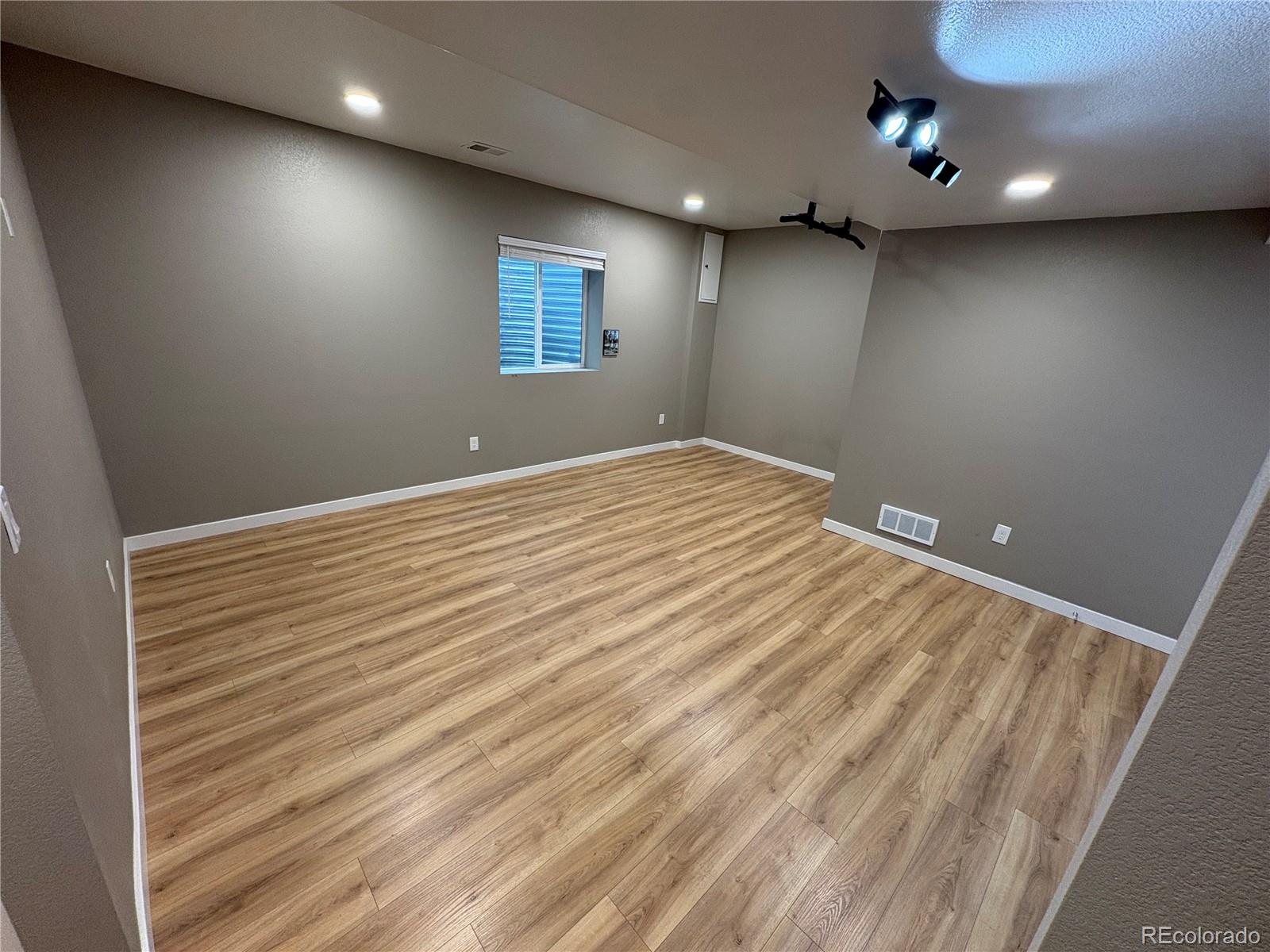 Vacant finished room with wood-look flooring, gray walls, a small window, and ceiling-mounted track lights.