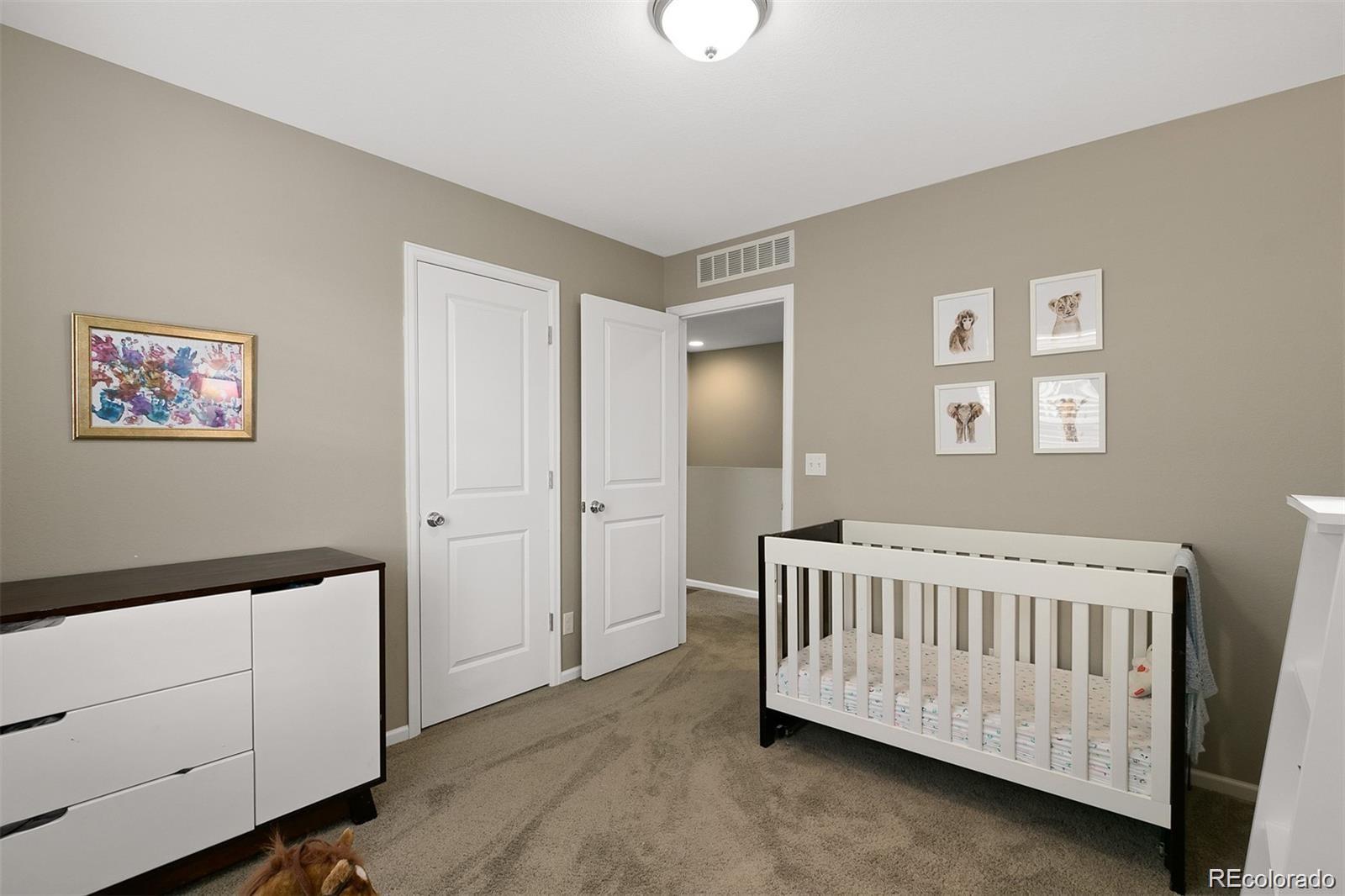 Nursery with a white crib, dresser, beige carpet, and framed animal prints.