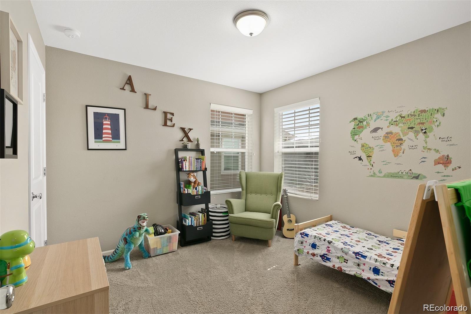 Child's bedroom with a world map mural, green chair, toys, and vehicle-print bedding.