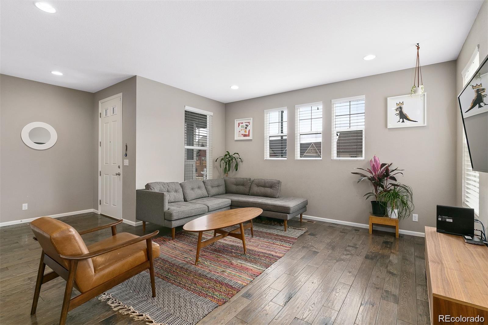 Living room with a gray sectional, leather armchair, patterned rugs, and bright windows.
