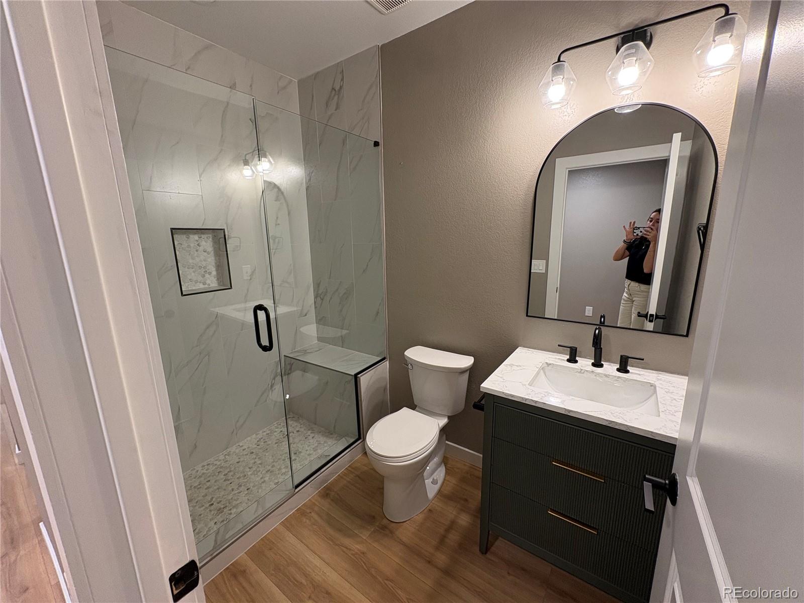 Bathroom with a glass walk-in shower, marble-look tile, and dark vanity.