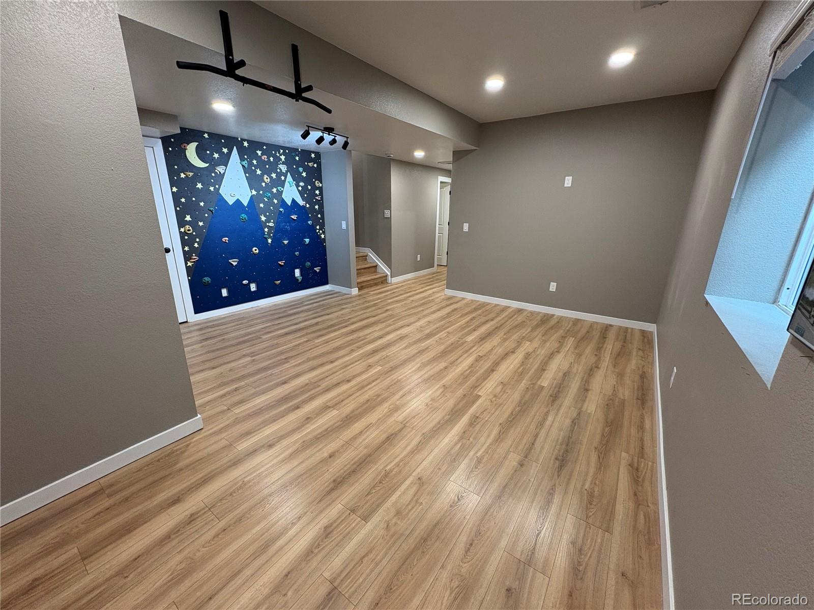 Finished room with wood-look floors and a blue mountain-themed climbing wall.