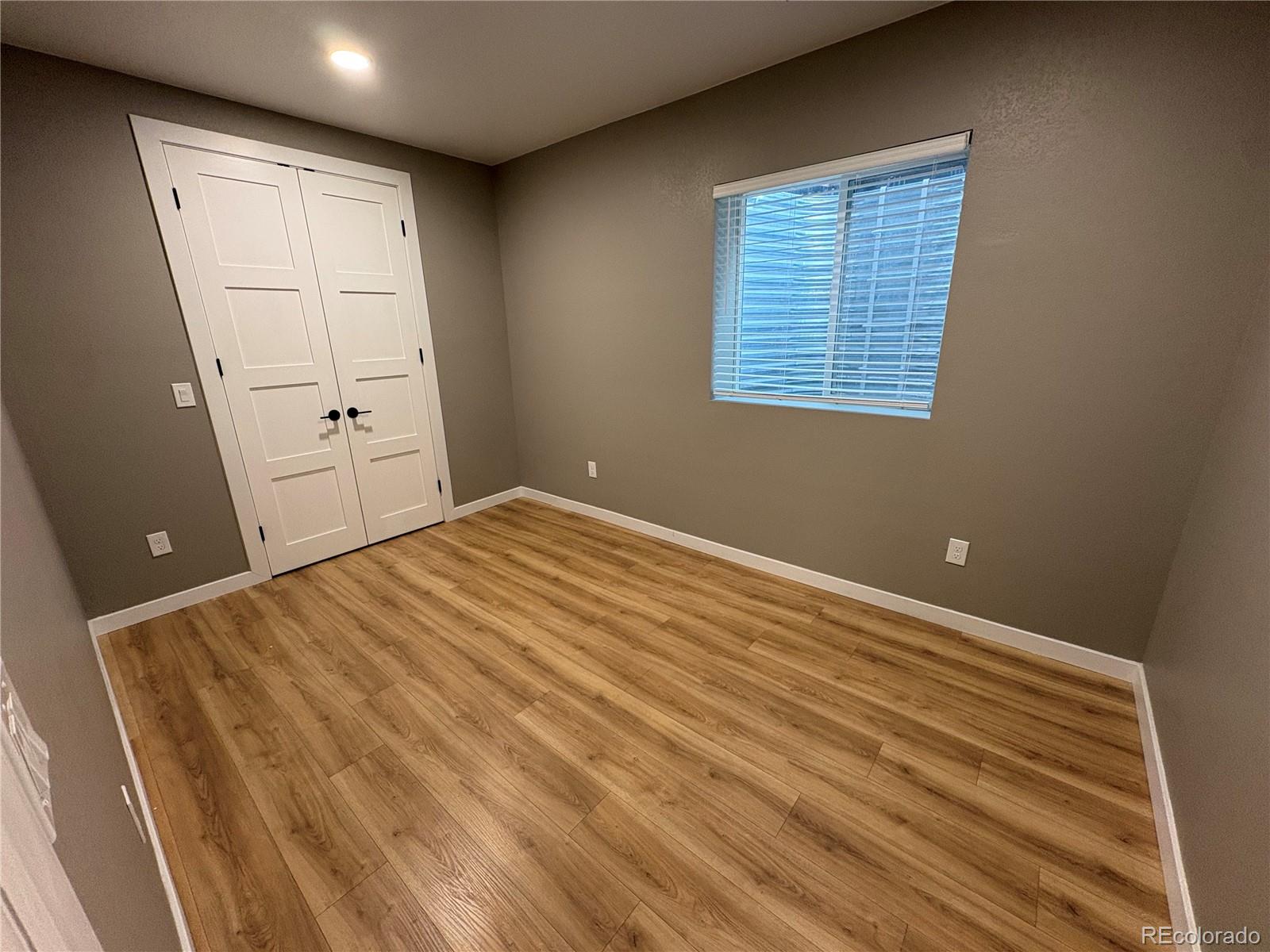 Empty room with white double closet doors, window blinds, and wood-look plank flooring.