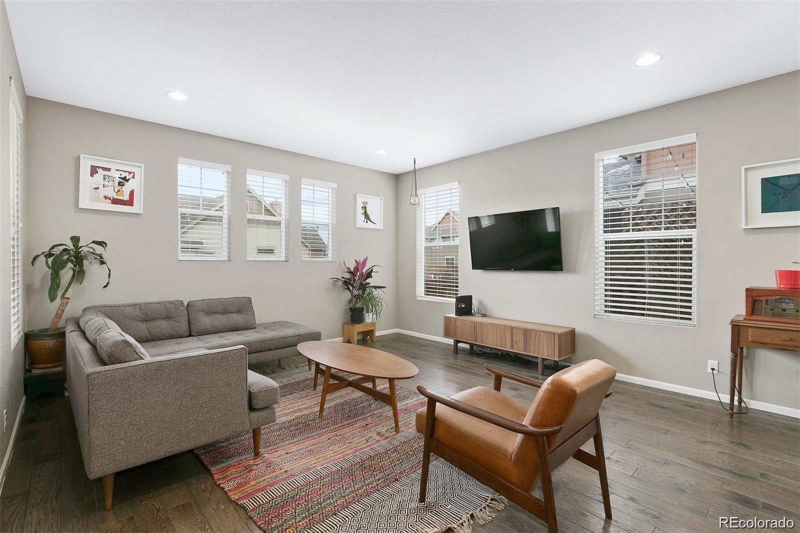Furnished living room with a gray sectional, leather chair, wall-mounted TV, and large windows.