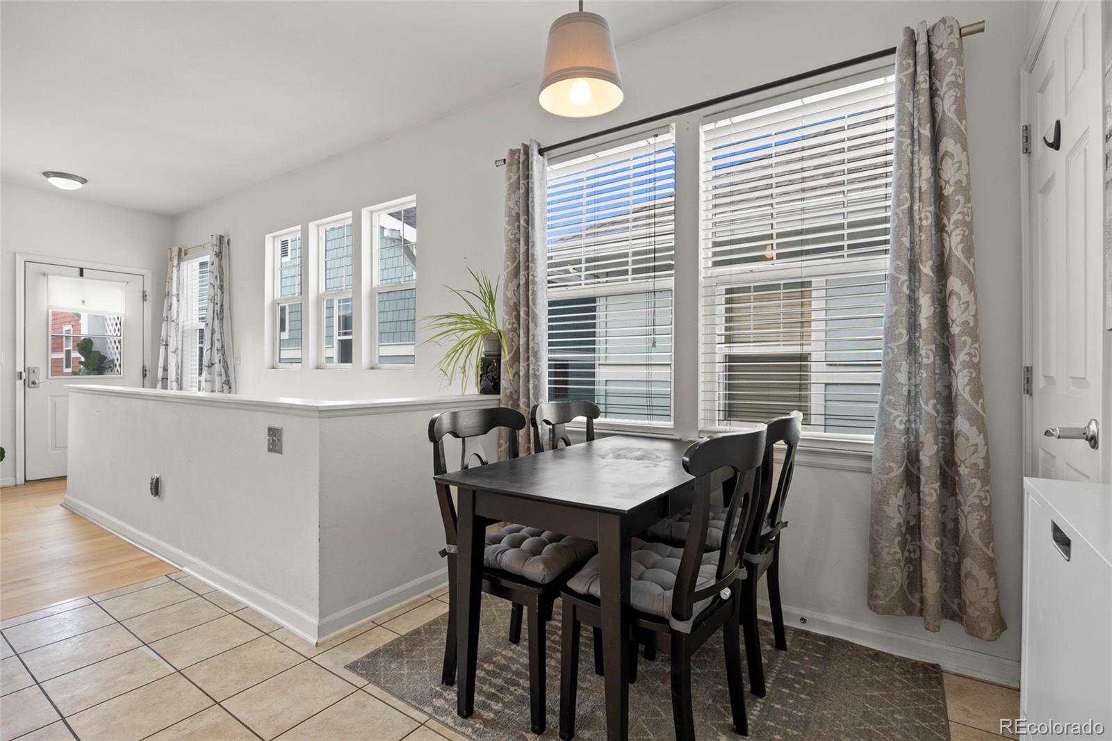 Dining area with a dark table and chairs beside large curtained windows.