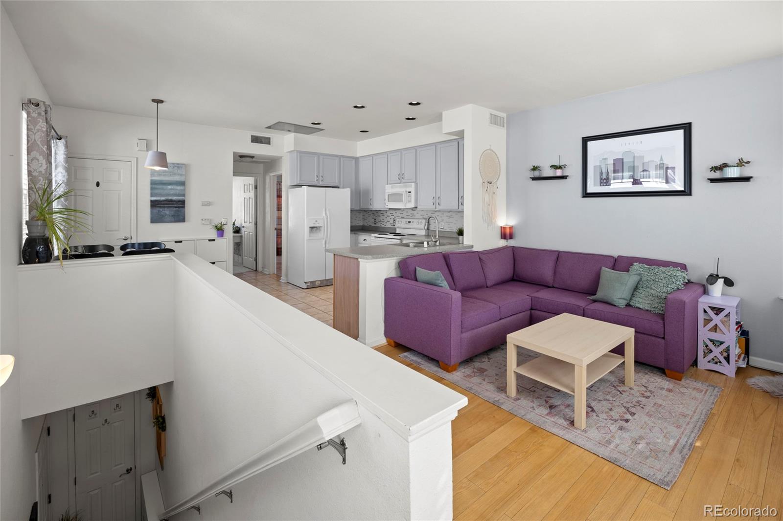 Open-plan living room and kitchen with a purple sectional, white cabinetry, and a stairwell.