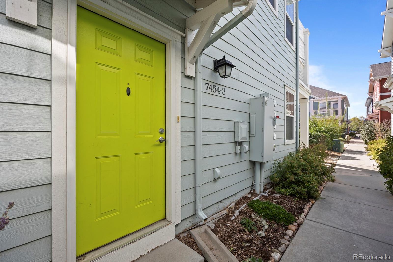 Unit entrance with a bright lime-green door, gray siding, and a landscaped walkway.