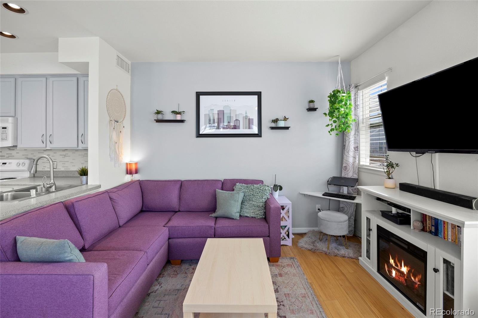 Living room with a purple sectional, wall-mounted TV, and fireplace beneath a white media console.