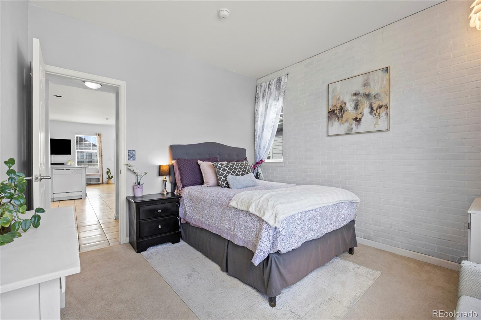 Furnished bedroom with a white brick accent wall and a bed beneath abstract artwork.