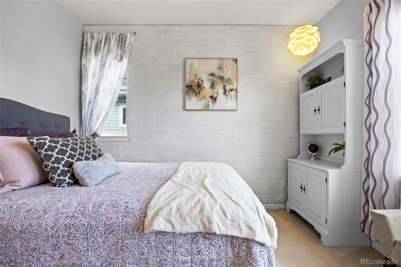 Bedroom with lavender patterned bedding, a white brick wall, and a built-in cabinet.
