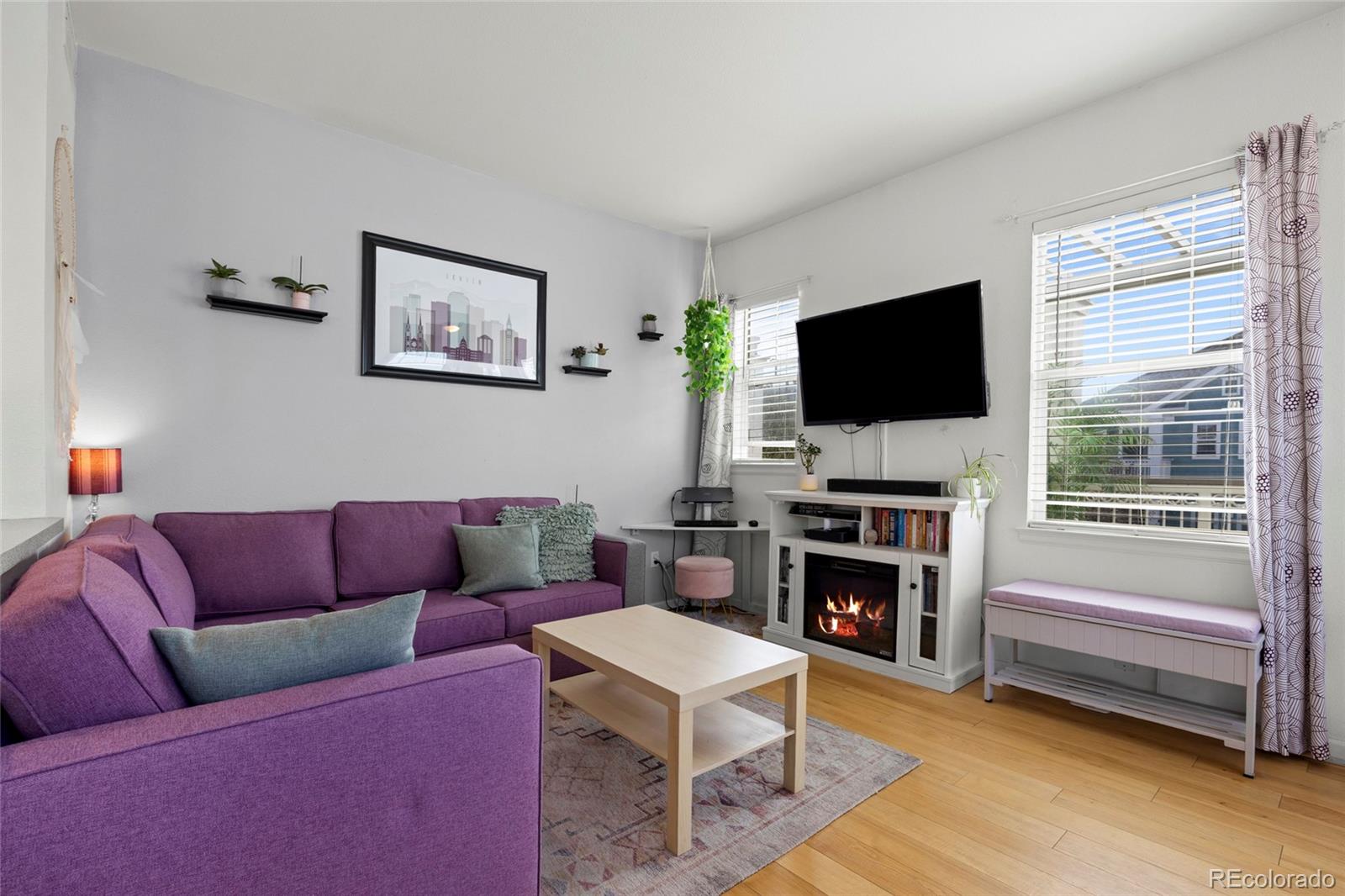 Living room with a purple sectional, lit fireplace, hardwood floors, and large windows.
