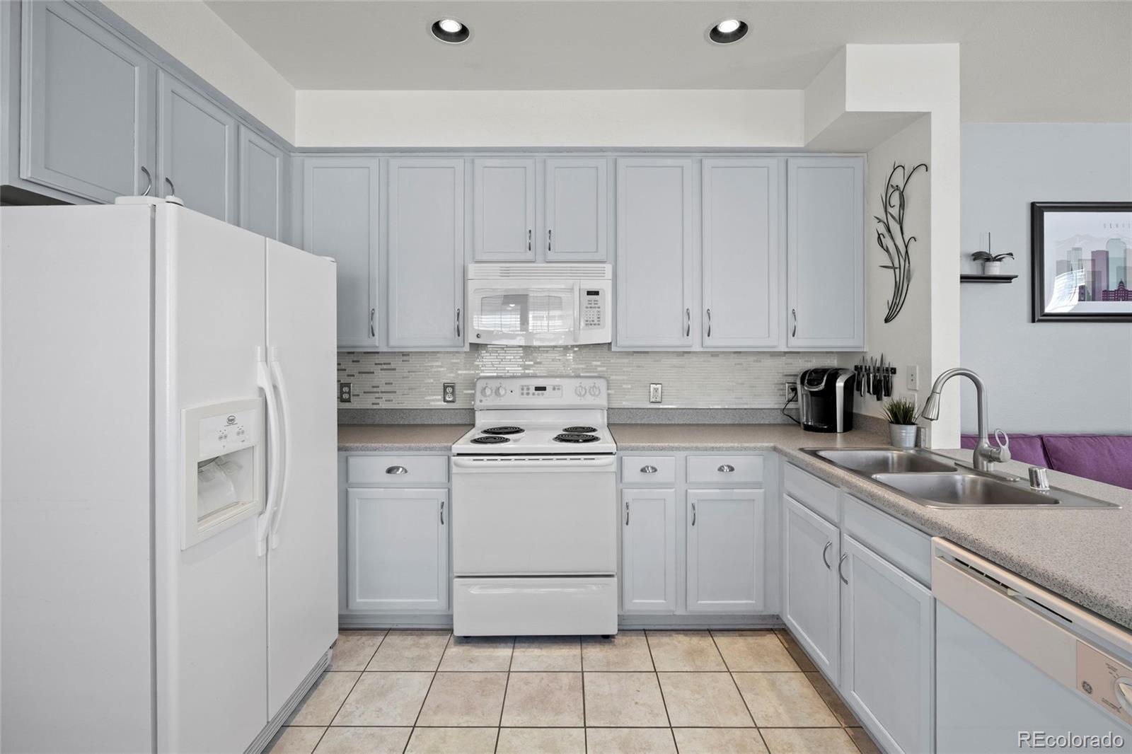 Kitchen with pale gray cabinets, white appliances, tiled backsplash, and a double-basin sink.