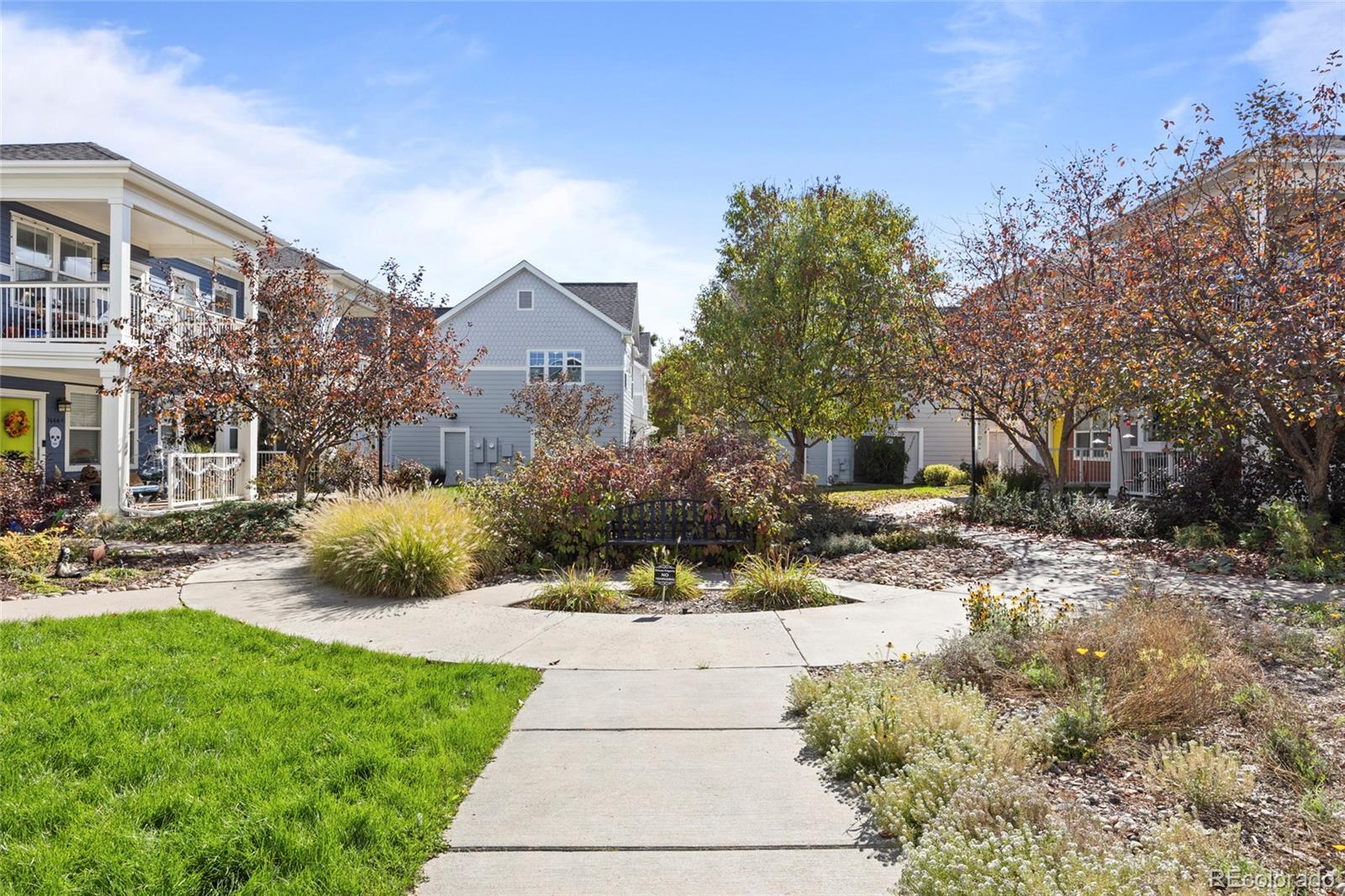 Townhome courtyard with a curved walkway, black bench, and autumn trees.