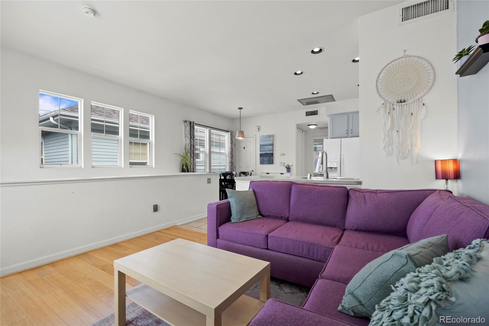Living room with a purple sectional sofa and an open kitchen with a breakfast bar.