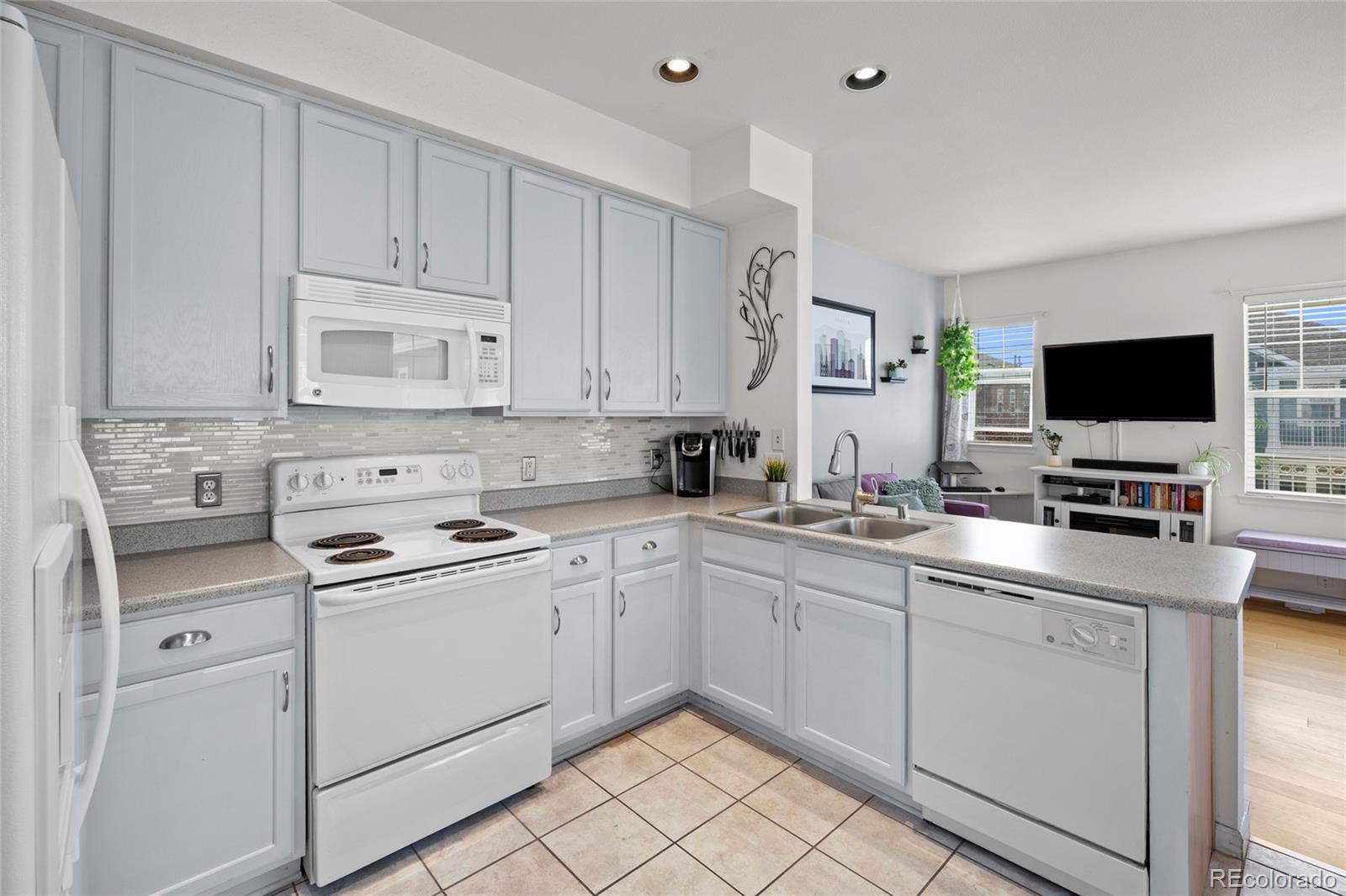 Kitchen with white cabinetry, tiled backsplash, and peninsula sink opening to the living area.