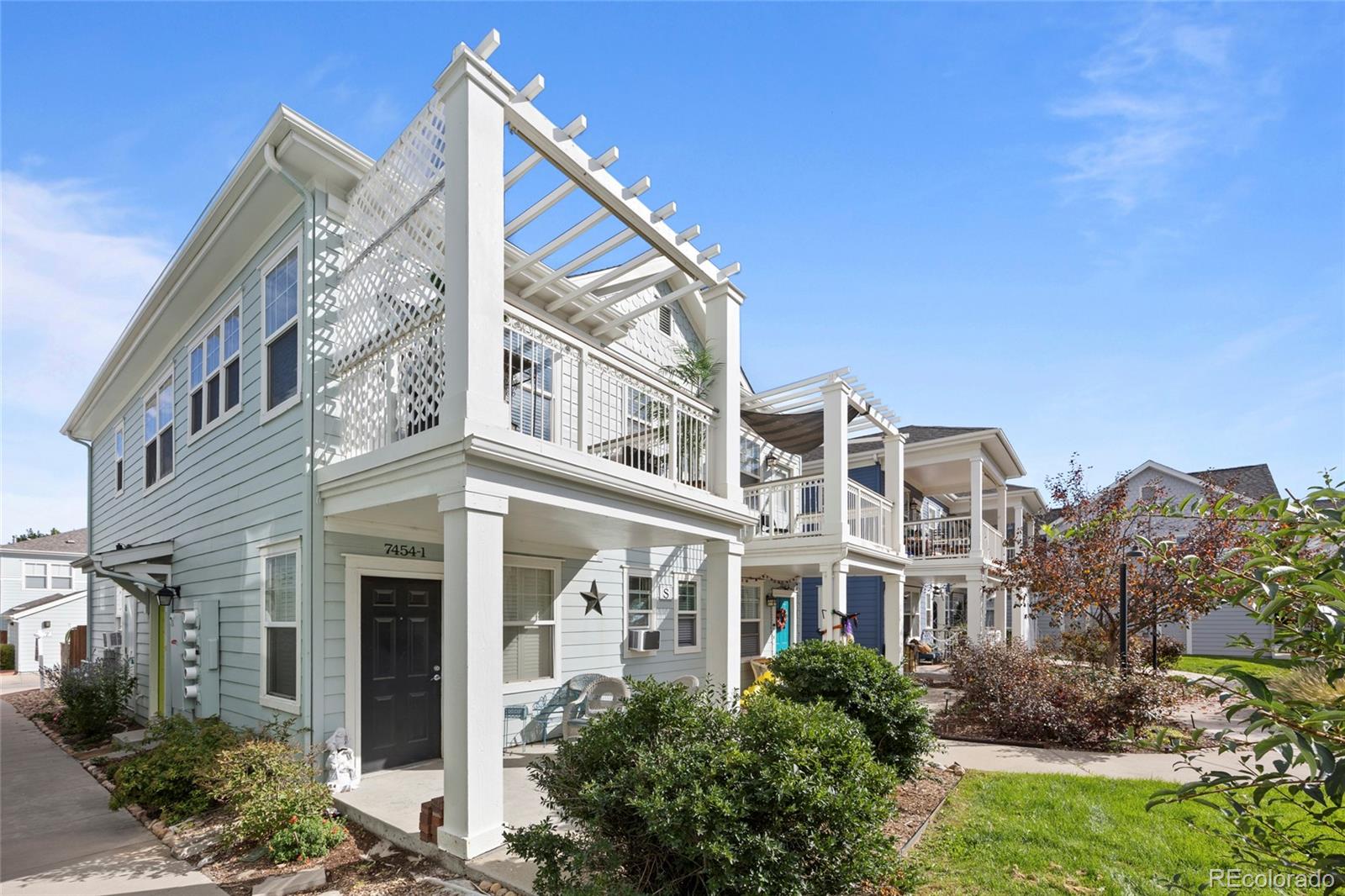 Pale blue townhouse with white pergola over an upper-level deck and landscaped front entry.