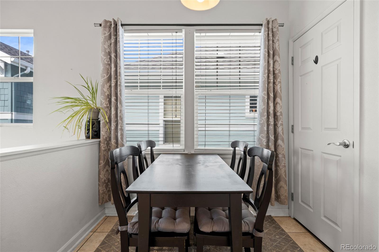 Dining area with a dark table and chairs in front of curtained windows with blinds.