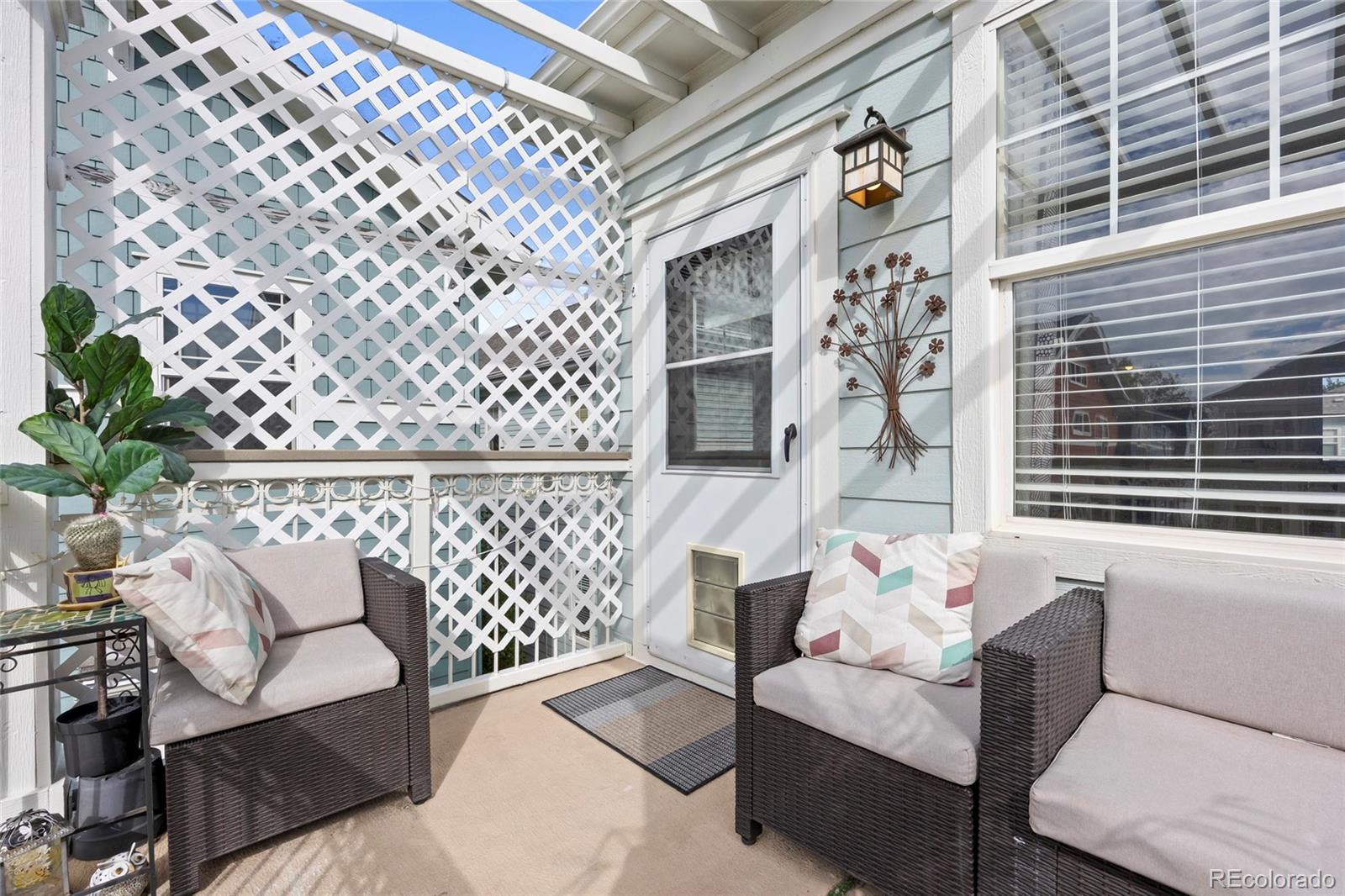 Patio seating beneath a white lattice trellis, with wicker chairs and a potted plant.