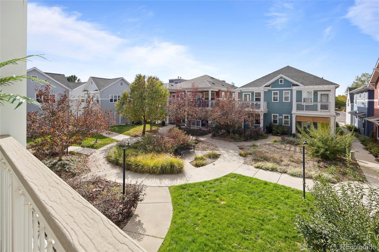 Landscaped courtyard with curved paths and a bench, seen from a balcony among two-story homes.