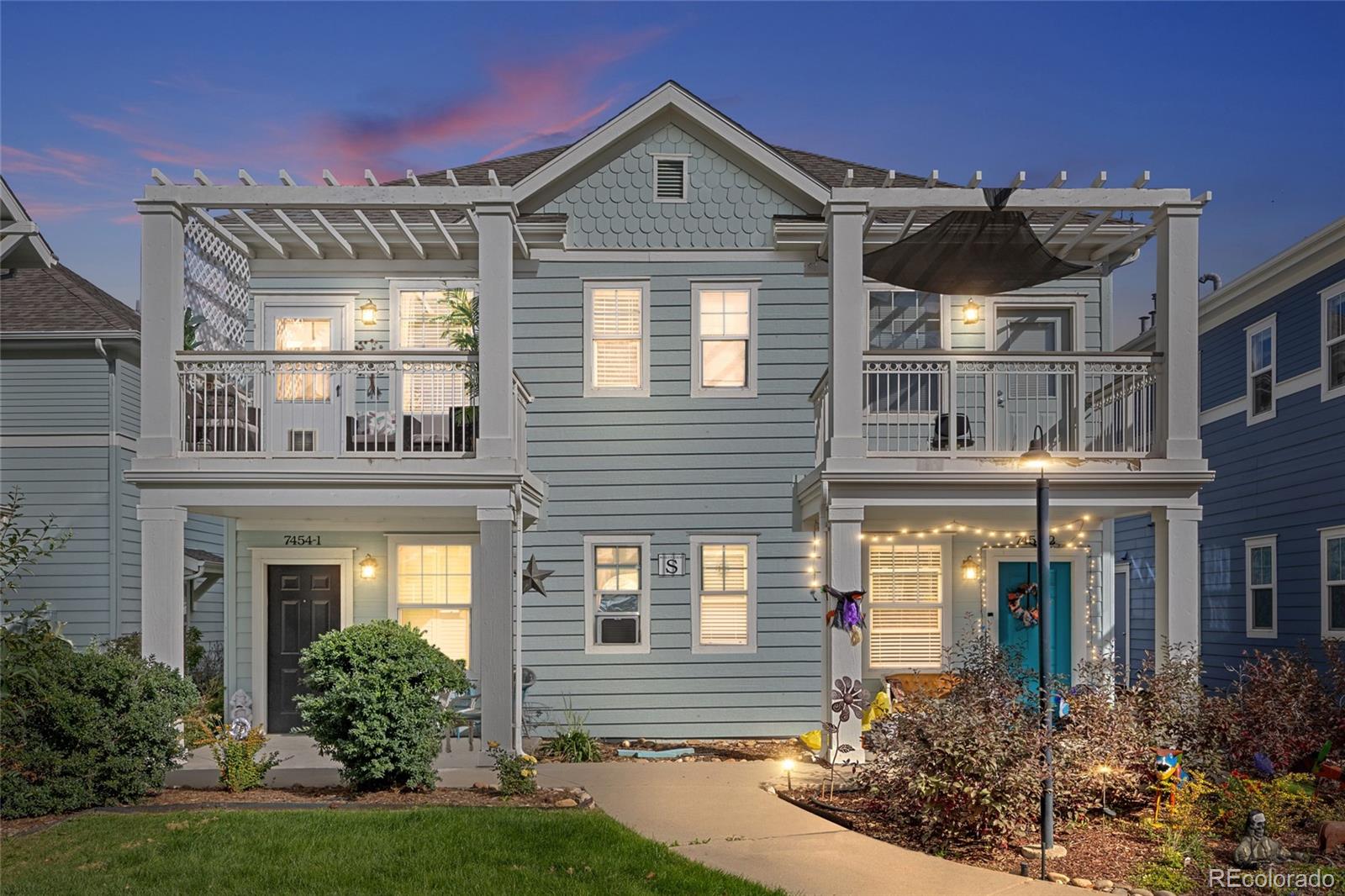 Blue-gray attached home with white pergola balconies and a landscaped front walk at dusk.