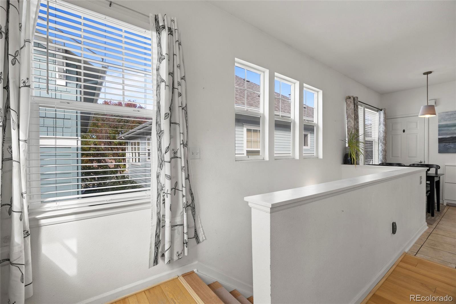 Bright stair landing with hardwood steps, a white half wall, and tall windows with blinds.
