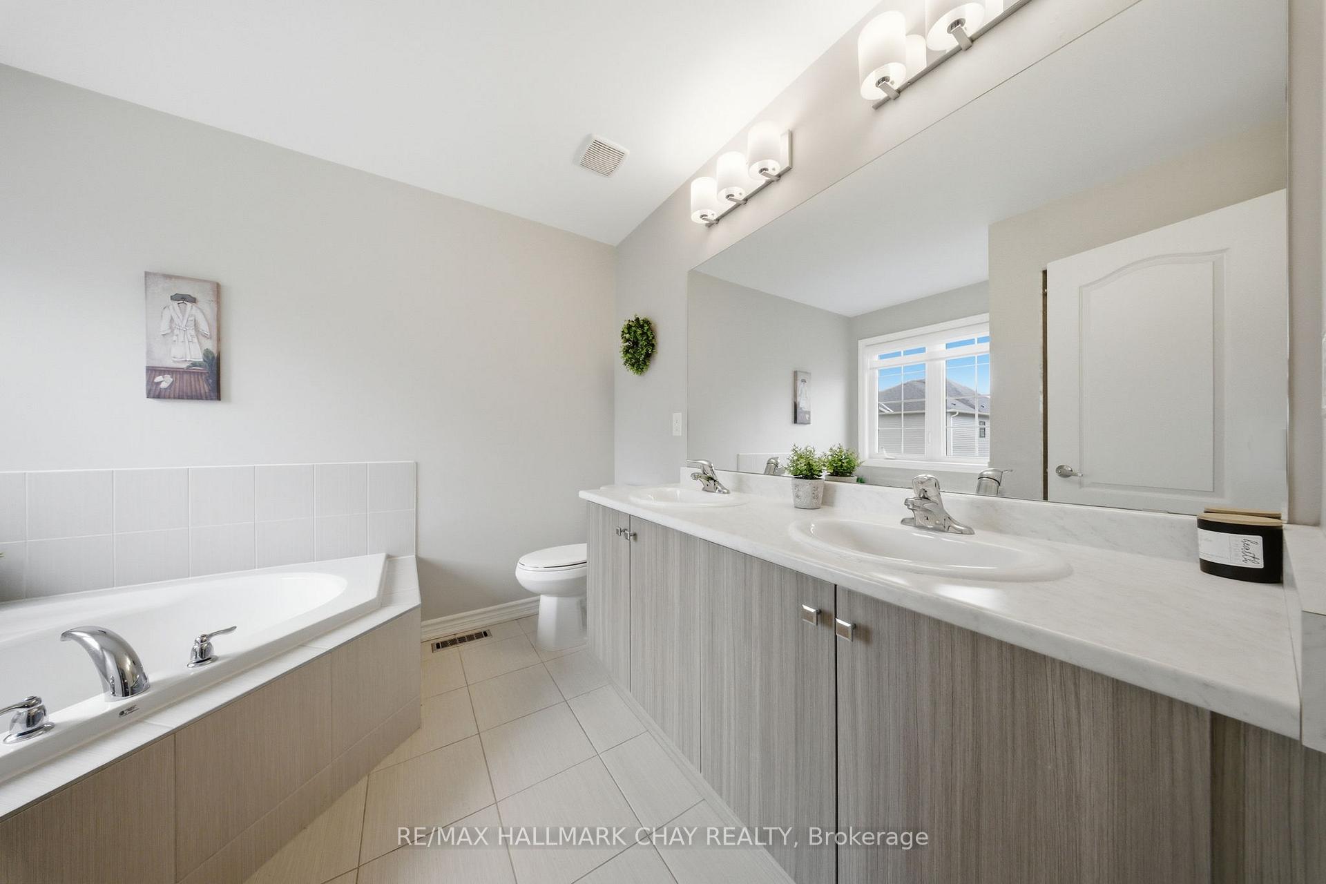 Bright bathroom with a built-in tub and long double-sink vanity beneath a large mirror.