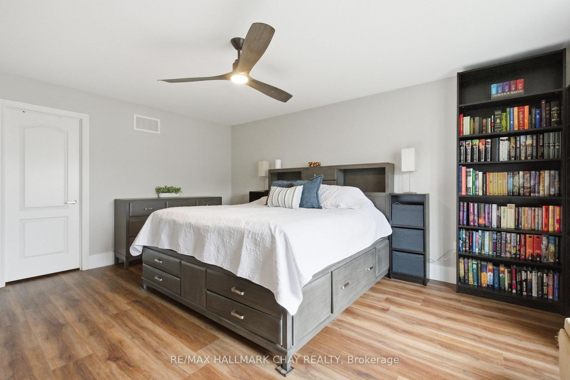 Furnished bedroom with a gray storage bed, blue pillows, and a tall bookcase filled with books.
