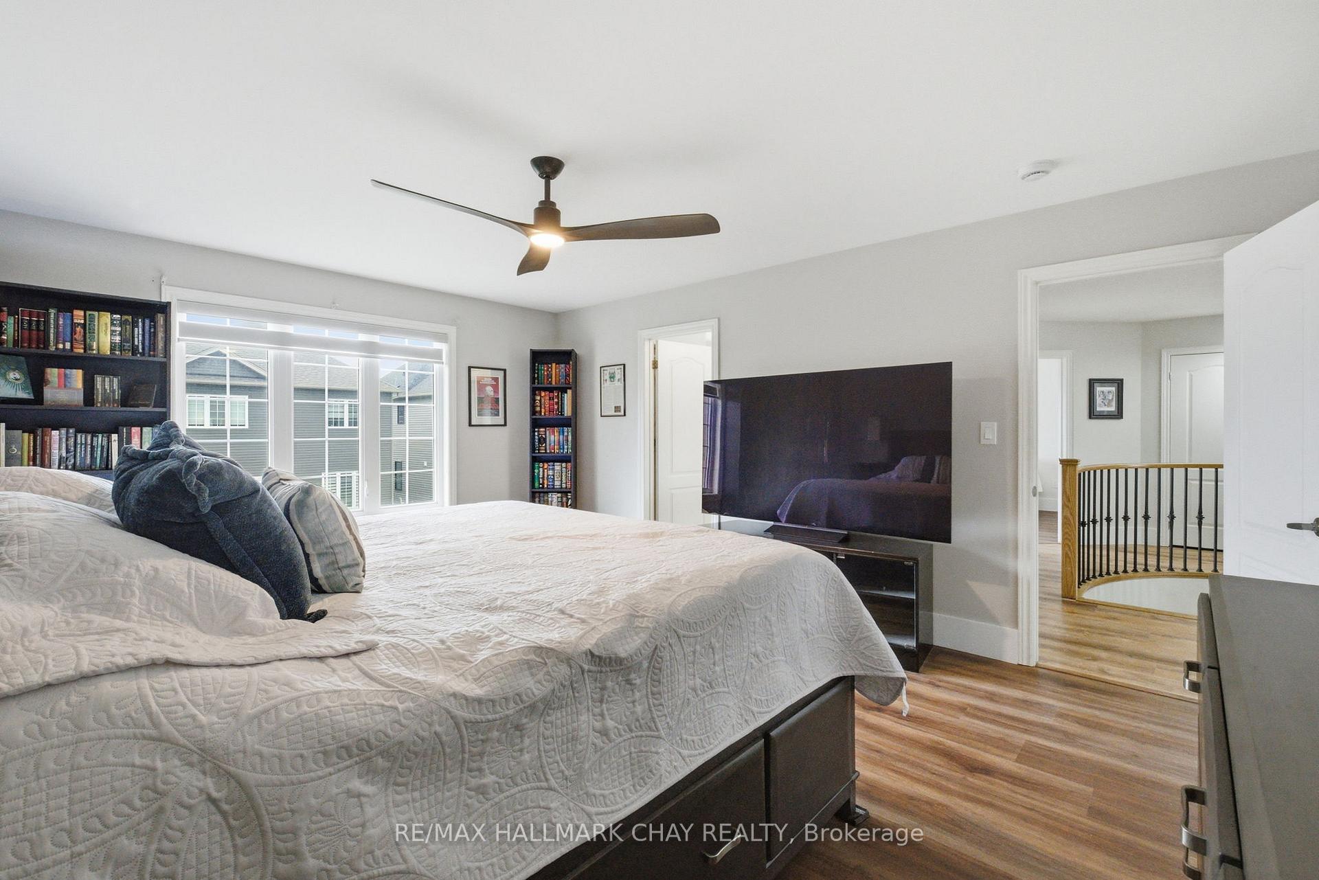 Furnished bedroom with a large bed, bookshelves, ceiling fan, and television beside a bright window.