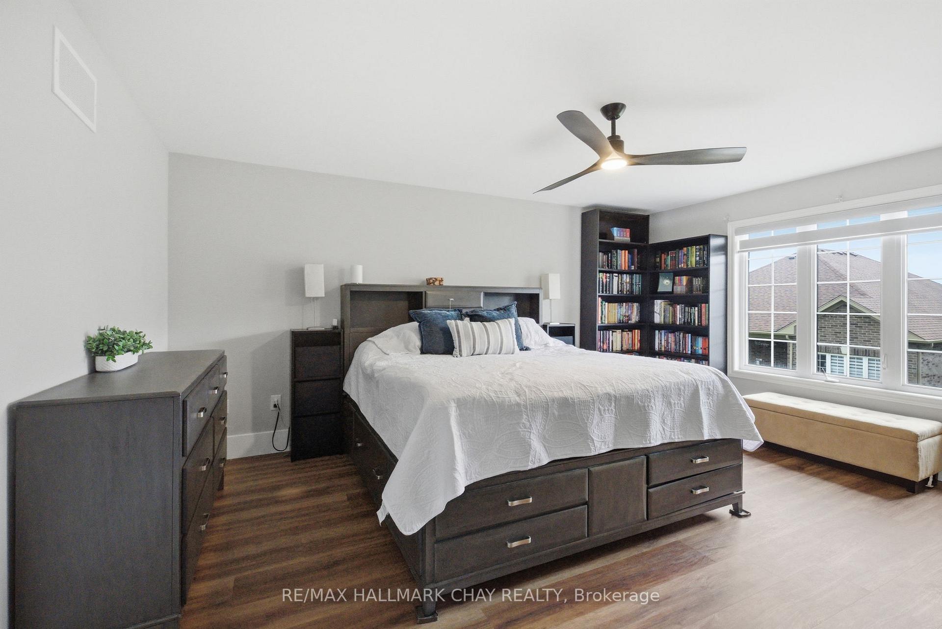 Furnished bedroom with a dark wood bed, tall bookcase, and large window with a cushioned bench.