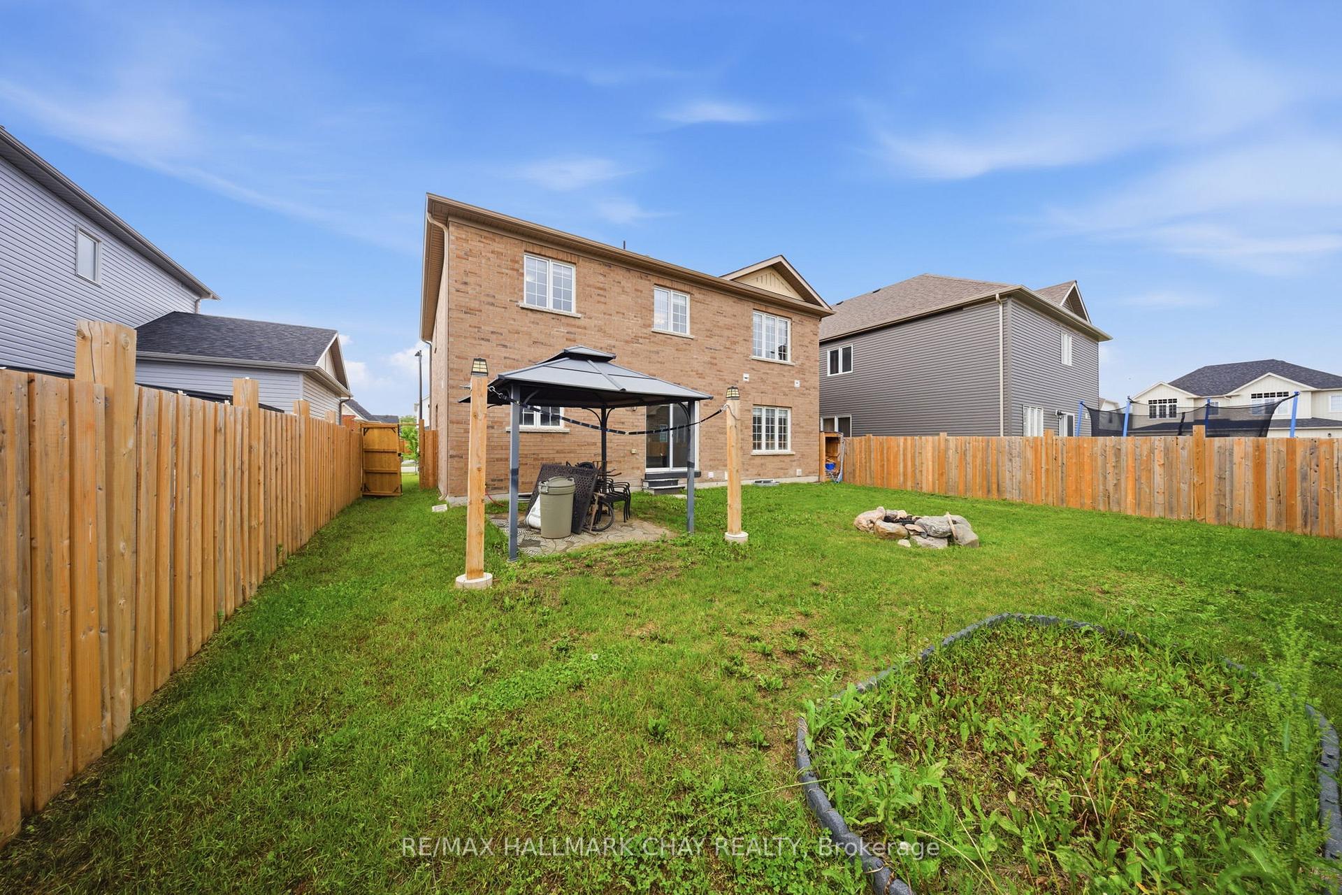 Fenced backyard with a gazebo, lawn, patio furniture, and fire pit behind a two-story brick house.