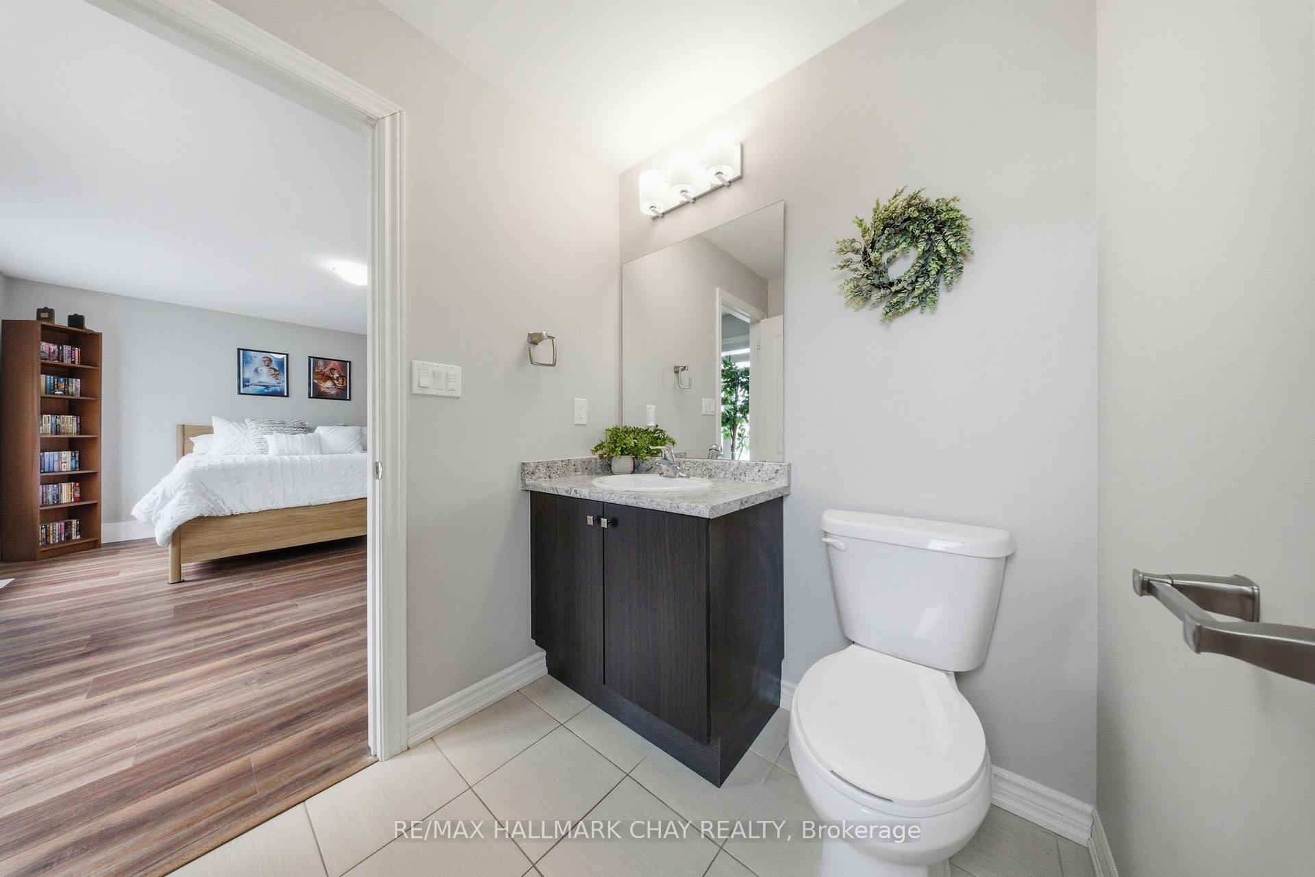 Bathroom with dark vanity and stone counter, opening to a bedroom with a white bed.