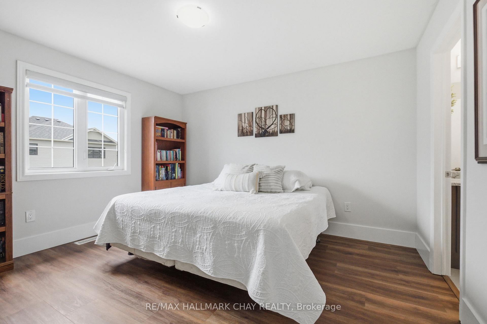 Furnished bedroom with a white quilted bed, large window, and dark wood flooring.