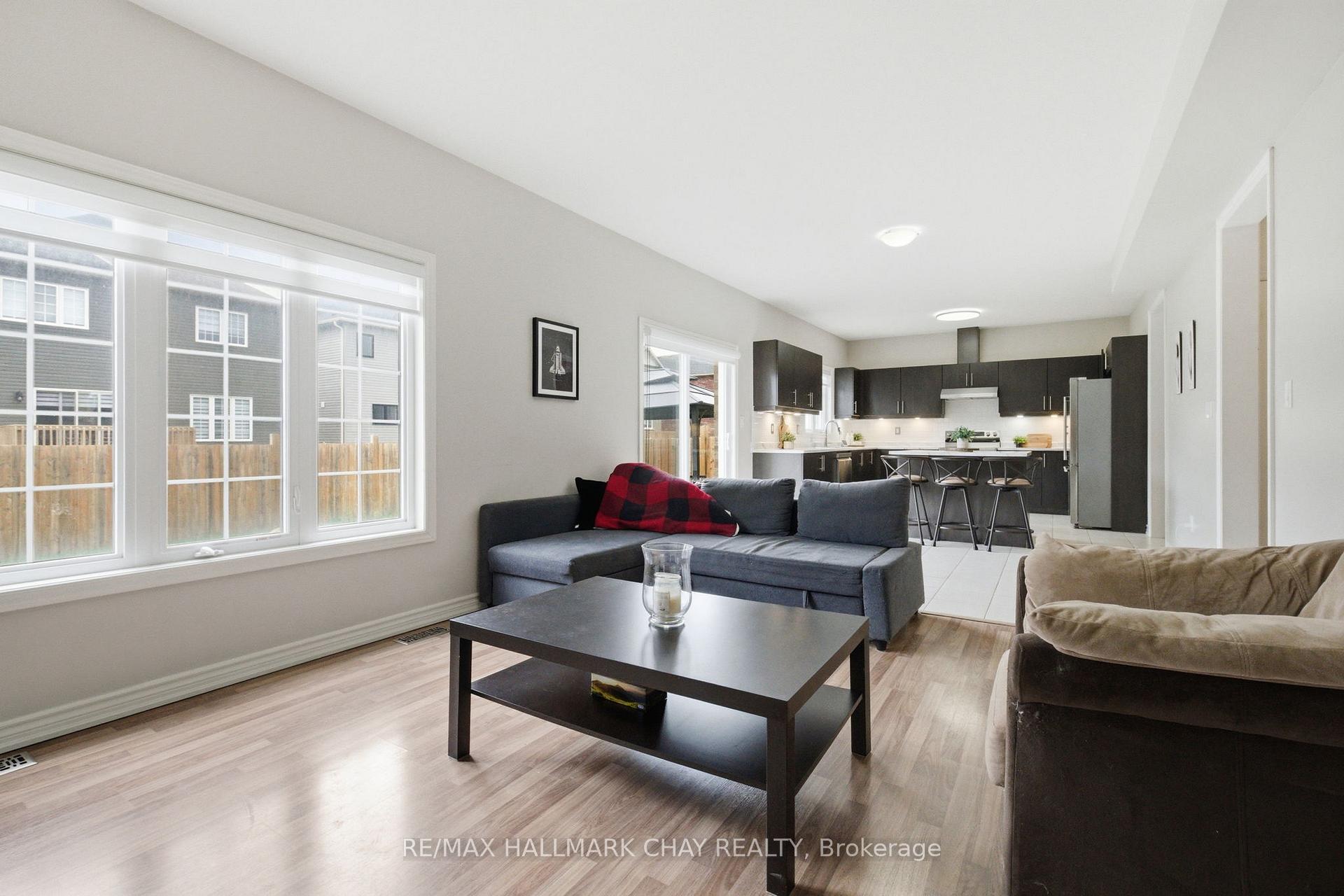 Open-concept living room and kitchen with a gray sectional, large windows, and dark cabinets.