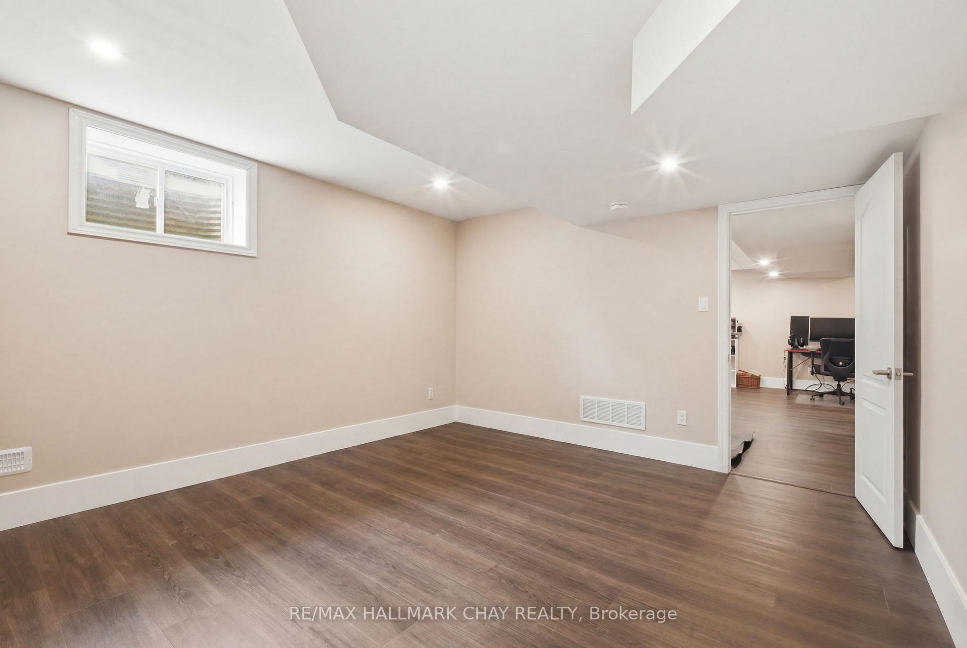 Empty basement room with dark flooring and an open doorway to a home office.