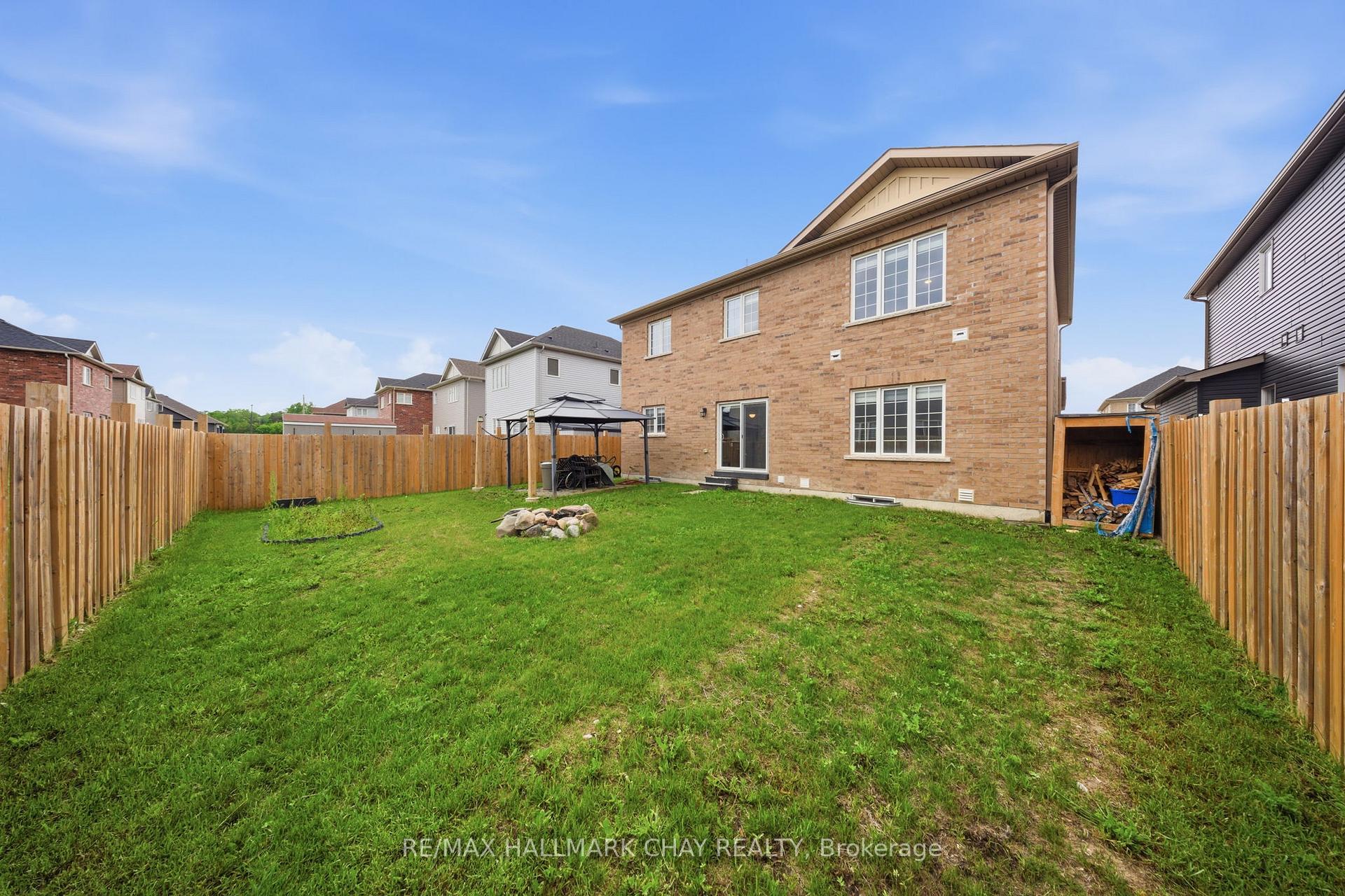 Fenced backyard with a broad lawn, brick house, gazebo, and small rock fire pit.