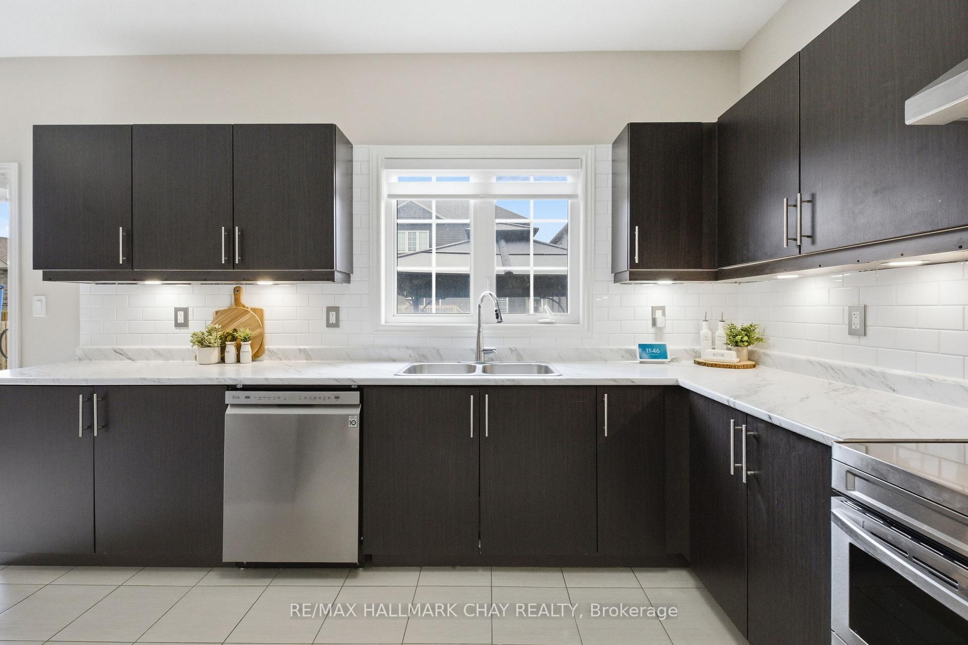 Modern kitchen with dark cabinets, white counters, and a double sink beneath the window.