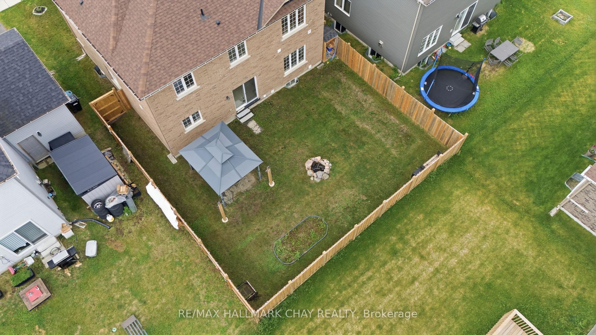 Aerial view of a fenced backyard with a gazebo, fire pit, garden bed, and trampoline.
