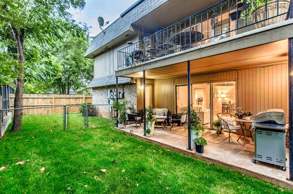 Two-story home with covered patio, upper balcony, and fenced grassy backyard.