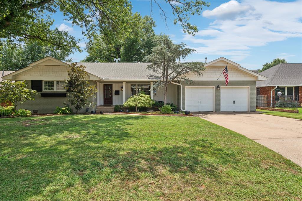 Single-story brick ranch with a two-car garage, American flag, and broad front lawn.
