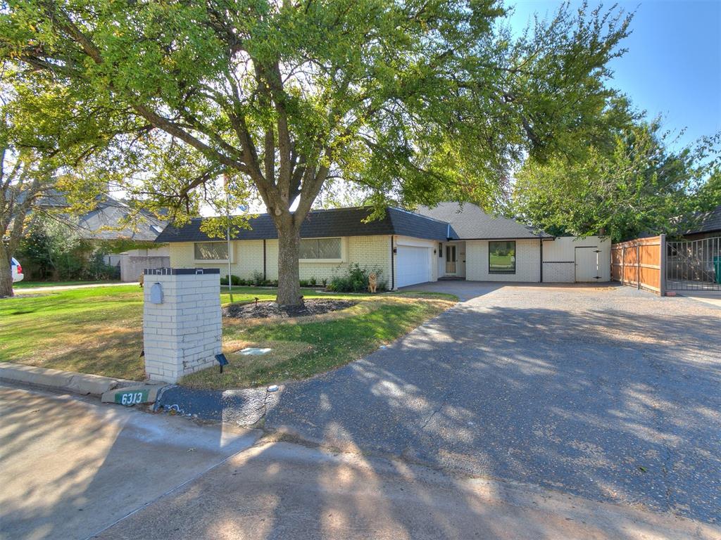 Single-story white brick house with an attached garage and mature shade trees.