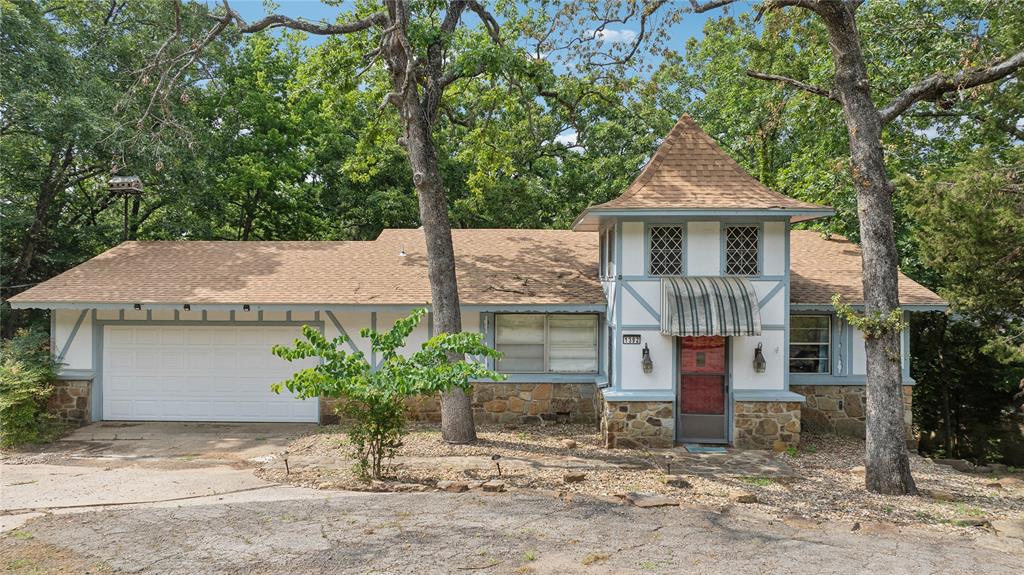House with a stone façade, red front door, attached garage, and mature shade trees.