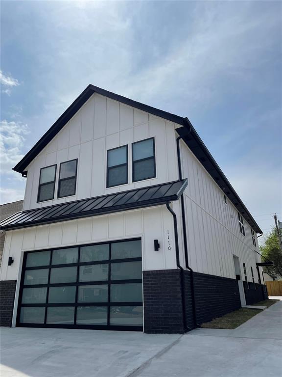 Modern white two-story home with black trim, dark brick lower walls, and a wide glass-panel garage door.