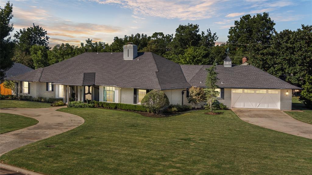 Single-story brick house with an attached two-car garage, curved driveway, and broad lawn at dusk.